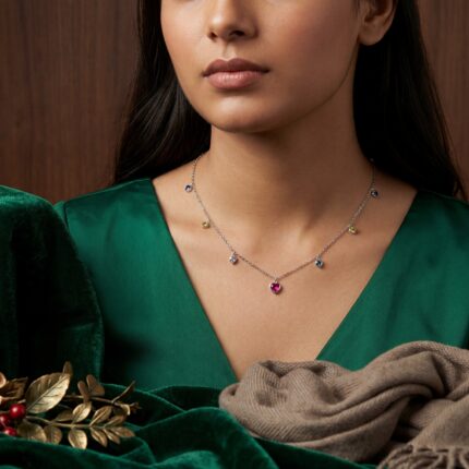 Woman modeling a Ekatva's sterling 925 silver heart necklace with colorful gemstone charms, elegant minimalist jewellery styling in emerald green outfit.